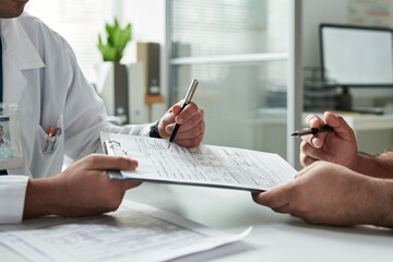 Middle aged Caucasian male patient consulting with doctor in medical office, both reviewing medical...