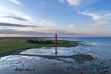 Arial view of a red and white lighthouse on the coast of Öland, Sweden surrounded by rugged...