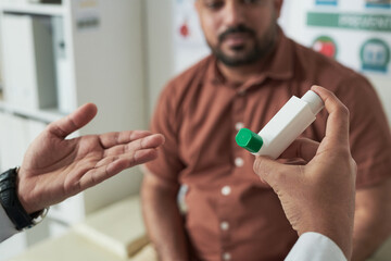 Middle aged Caucasian man sitting in medical office consulting with doctor, doctor holding inhaler...