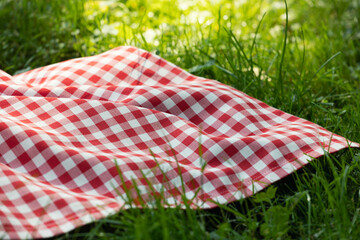 Red picnic cloth on grass closeup.Empty food advertisement place background.Checkered tablecloth outdoors, checked towel plaid.