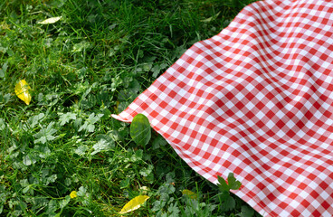 Red picnic cloth on grass closeup.Empty food advertisement place background.Checkered tablecloth outdoors, checked towel  plaid.
