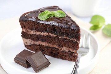 Piece of delicious cake, mint, chocolate and fork on light table, closeup