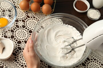 Woman whisking cream with hand mixer at table, above view