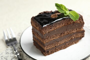 Piece of chocolate cake served with mint and fork on table, closeup