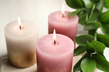Burning candles and green leaves on white table, closeup
