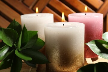 Burning candles and green leaves on wooden tray, closeup