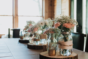 Row of rustic mason jar vases on wood slice pedestals filled with pink carnations, white daisies...