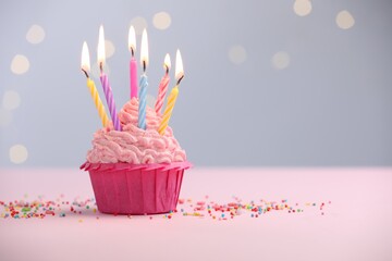 Burning candles in cupcake and sprinkles on table against blurred lights. Space for text