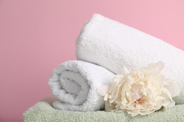 Stack of soft towels and peony flower on pink background, closeup