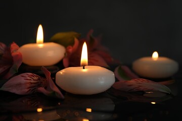 Burning candles and beautiful flowers on wet black table, closeup. Space for text