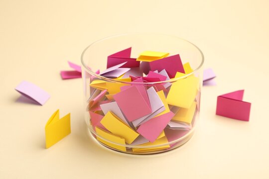 Jar with colorful pieces of paper on beige background, closeup