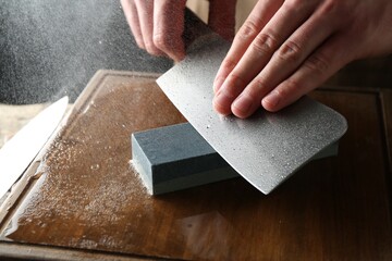 Man sharpening knife with sharpener on wooden table, closeup