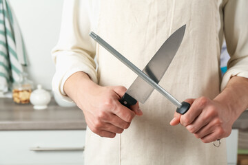 Man sharpening knife with sharpener indoors, closeup