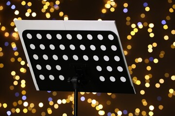 Note stand with music sheets against blurred lights, closeup. Bokeh effect