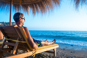 Man is relaxing on a sun lounger in the rays of the setting sun. Summer beach vacation. Himare....