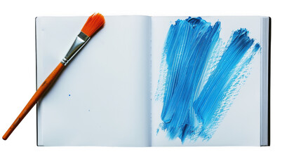 A paintbrush rests beside a vibrant blue paint stroke on the open page of a notebook isolated on white background