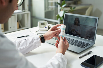 Middle aged Caucasian male doctor holding medication bottle during telemedicine consultation with young adult Black woman patient on laptop screen, discussing diabetes treatment options