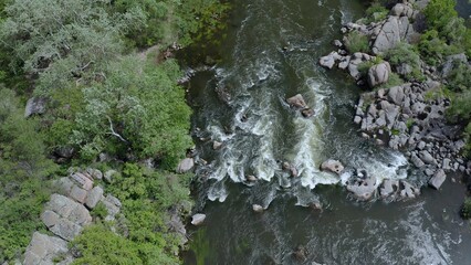 Aerial view of a turbulent stream in the mountains. Gusts of wind swaying tree branches.