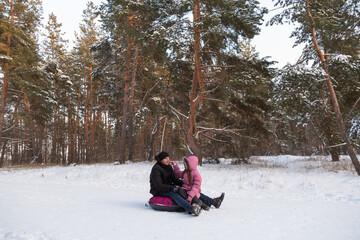 Father and daughter having fun with snow tube in the forest