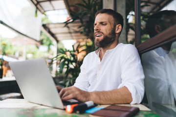 Bearded freelancer reacting emotionally while working on laptop, reflecting frustration in...