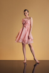 Confident woman poses in a short pink organza cocktail dress featuring layered frills and a large...