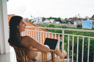 Smiling freelancer woman enjoys tech-enabled remote lifestyle on tropical balcony, showcasing joy,...
