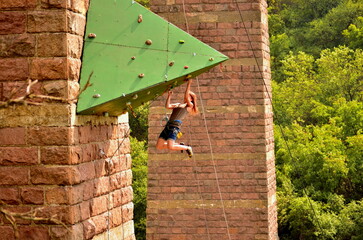 Horizontal photo capturing a dynamic moment of a woman hanging from a green artificial climbing...