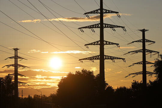 Silhouettes of high voltage towers with electrical wires on background of sunset sky. Electricity transmission lines in city, power supply concept