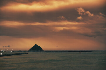 Long pier at the harbour of New Plymouth, New Zealand, just after sunset. The pyramid-shaped rock is called Whareumu (Lion Rock)
