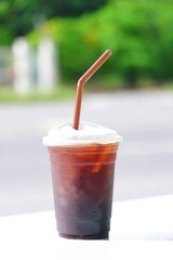 A cup of iced Americano on the white table with blurred green nature background 