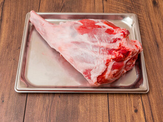 Fresh raw leg of lamb is on a silver stainless tray which is on a wooden table. Premium high...