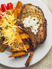 A plate of food with a premium pork chop in the bone, wedges potatoes, and tomatoes and cheddar...