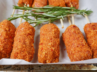 Fancy kebabs on wooden sticks and fresh rosemary fresh herb on cooking paper in a cooking tray on wooden table. Popular food made of beef or lamb mince.