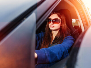 A young inexperienced woman is driving a car with her sunglasses on. She is wearing a blue hoodie....