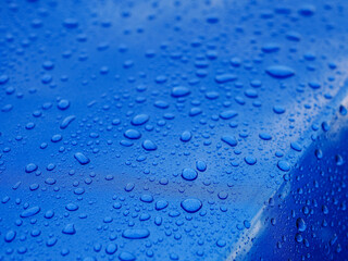 The image is of a blue surface with many small drops of water on it. The drops are scattered all...