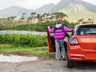 Young teenager girl standing by small red sport car and enjoys view of Twelve pines island and...