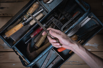 Top-down view of old beige wooden table with chipped paint showing hand holding vintage metal file...