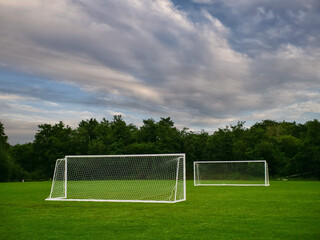Clean cut football or soccer training ground with two goal posts, dark trees and dramatic sky in...
