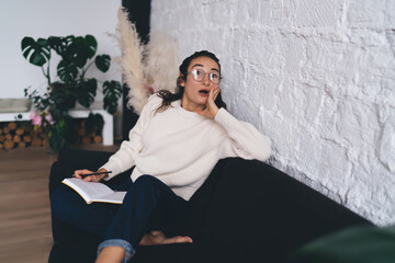 Freelancer in casual outfit sits surprised, holding notebook and pen, capturing sudden inspiration...