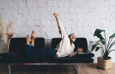 Excited freelancer raises hand in cheerful celebration while working remotely on laptop, expressing...