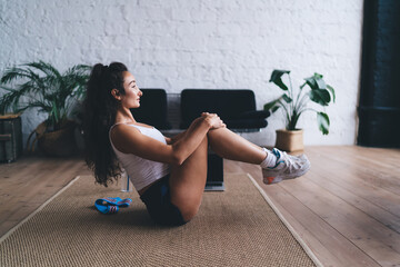 Relaxed tech-assisted recovery moment after virtual workout, woman hugging knees while syncing...