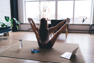 Focused sit-up crunches led by virtual trainer on laptop, woman performs core activation routine...