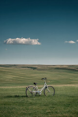 Obraz premium electric bicycle standing in endless green field under clear blue sky with light cloud