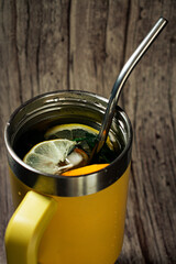 A yellow insulated travel mug filled with a refreshing drink, garnished with lemon and orange slices and a metal straw. Perfect for showcasing healthy beverages, eco-friendly habits, or cozy moments.