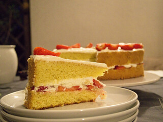 Strawberry cake slice with whipped cream and fruit in focus, full cake visible behind, showing rich layers and texture.