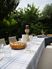Peaceful garden table setting with light patterned cloth, vintage wooden candle holders, glassware, and cutlery—surrounded by lush greenery.