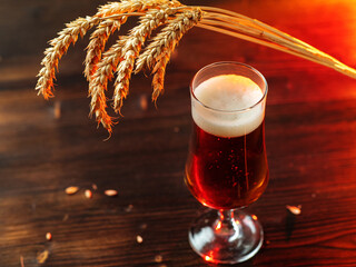 Light beer glass on wooden table, ears of wheat
