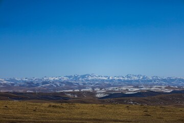 Snow-capped mountains stretch across the vast grassland near Ngawa in the historical Amdo region of Tibet, showcasing the serene high-altitude landscape of the Tibetan Plateau.