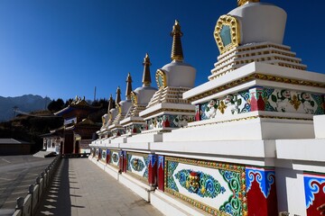 Colorful line of Tibetan stupas at Taktsang Lhamo Monastery in Langmusi, Amdo region, showcasing intricate Buddhist art and traditional Himalayan architecture.
