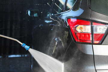 Using a pressure washer at a car wash on a sunny day, washing a car at a self-service station (part...